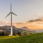 Wind turbine amid rolling hills and mountains at sunset, symbolizing renewable energy and sustainability.