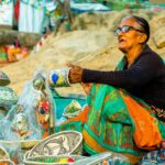 Elderly woman selling colorful traditional handicrafts at an outdoor market.