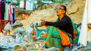 Elderly woman selling colorful traditional handicrafts at an outdoor market.