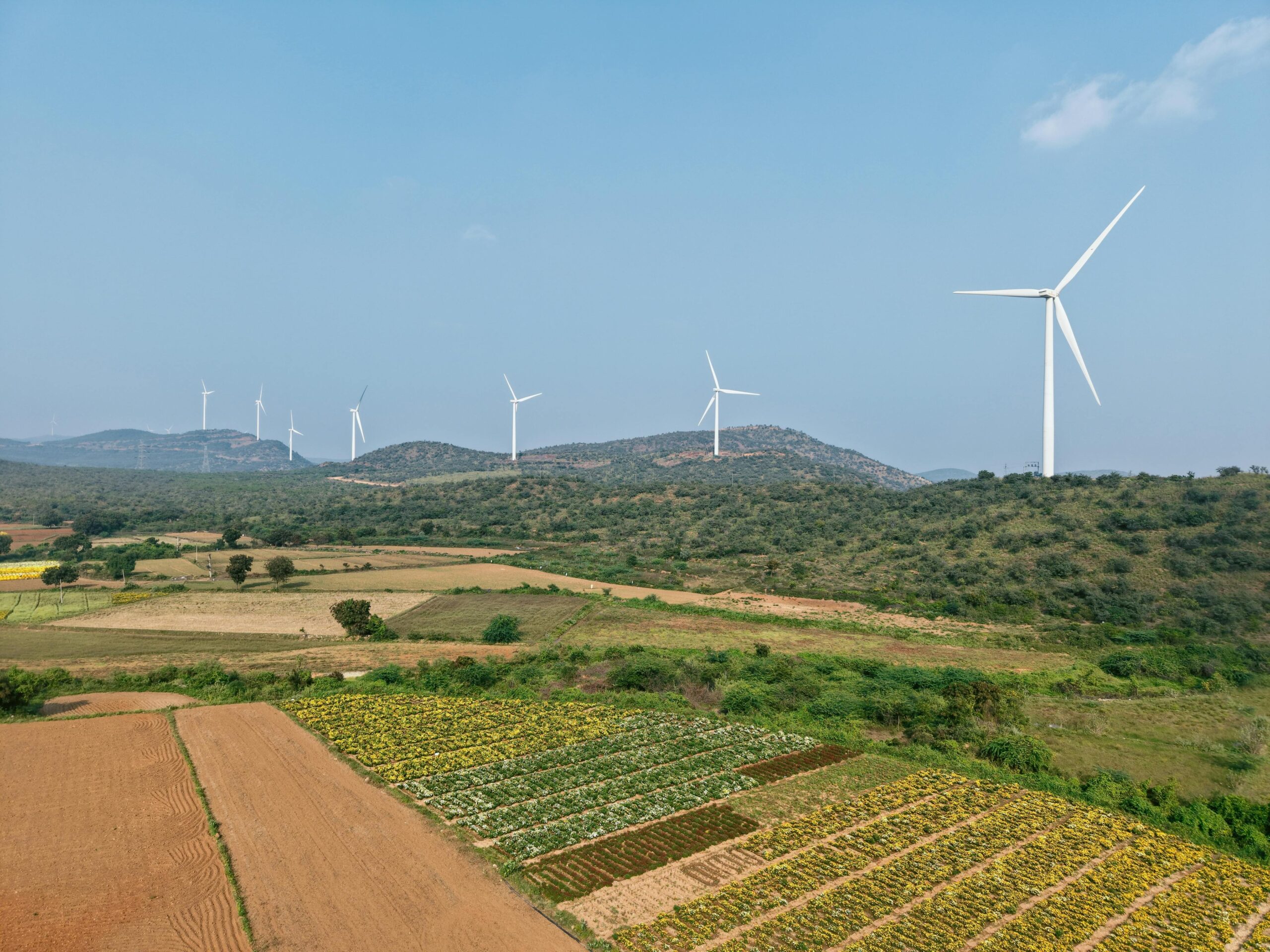 Aerial view of wind turbines in a lush rural landscape under clear blue skies.