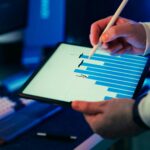 A person using a stylus on a tablet showing a business graph in an office setting.