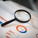 An image showcasing a magnifying glass placed on financial graphs and charts depicting statistical data.