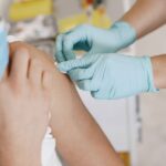 Close-up of a nurse wearing gloves giving an injection to a patient wearing a mask.