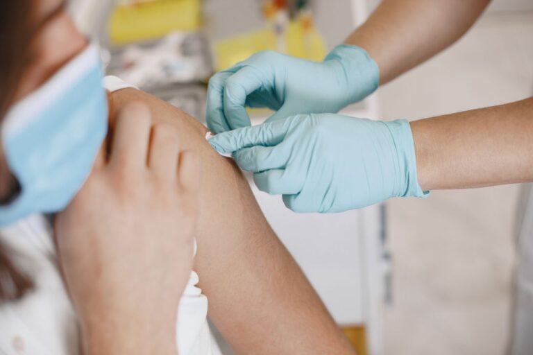 Close-up of a nurse wearing gloves giving an injection to a patient wearing a mask.