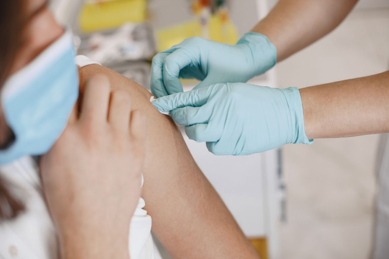 Close-up of a nurse wearing gloves giving an injection to a patient wearing a mask.