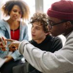 Three young adults discussing content on a smartphone indoors.